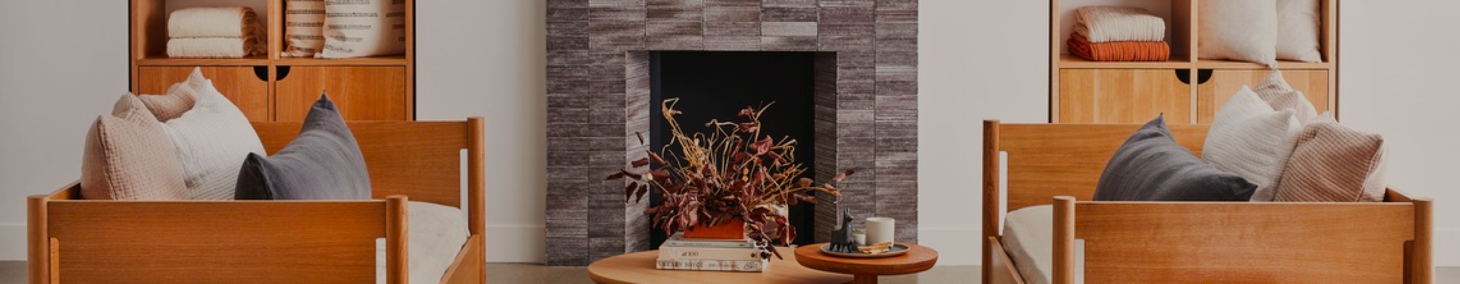 A living room scene with a fireplace, coffee table, couches, and shelving. The decor is light and airy.