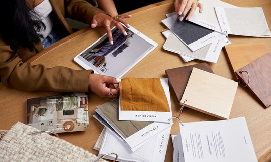 Two people sit at a table looking through fabric swatches and photographs 