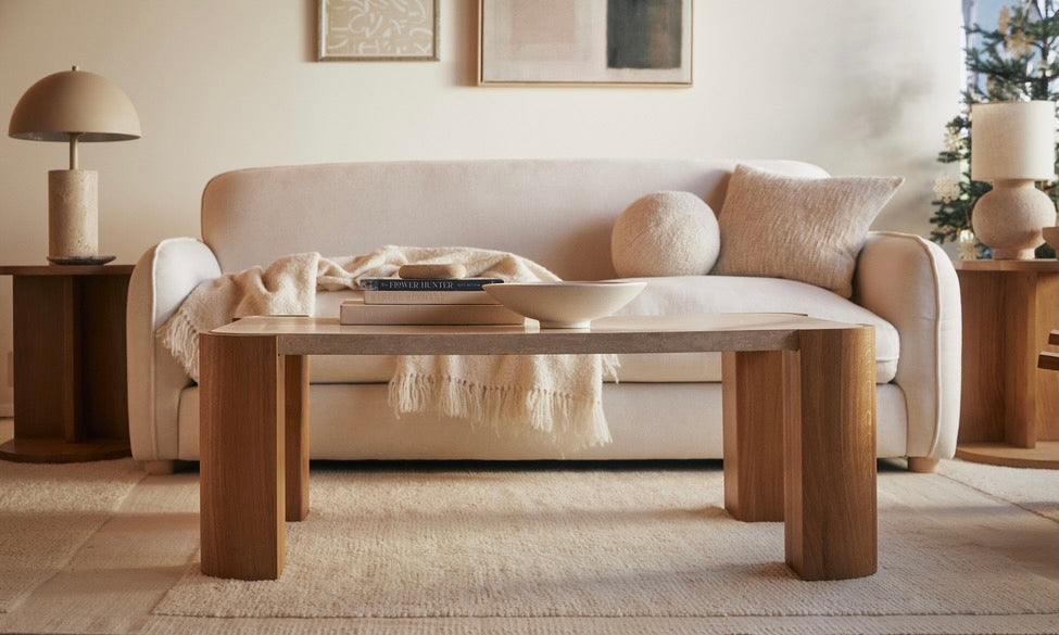 A living room scene shows a coffee table in the foreground, with a couch and side tables behind. The color scheme is cream and beige. 