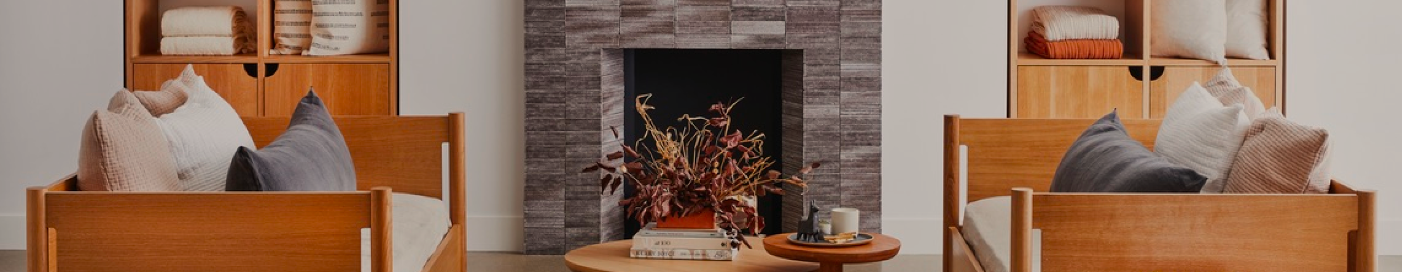 A living room scene with a fireplace, coffee table, couches, and shelving. The decor is light and airy. 